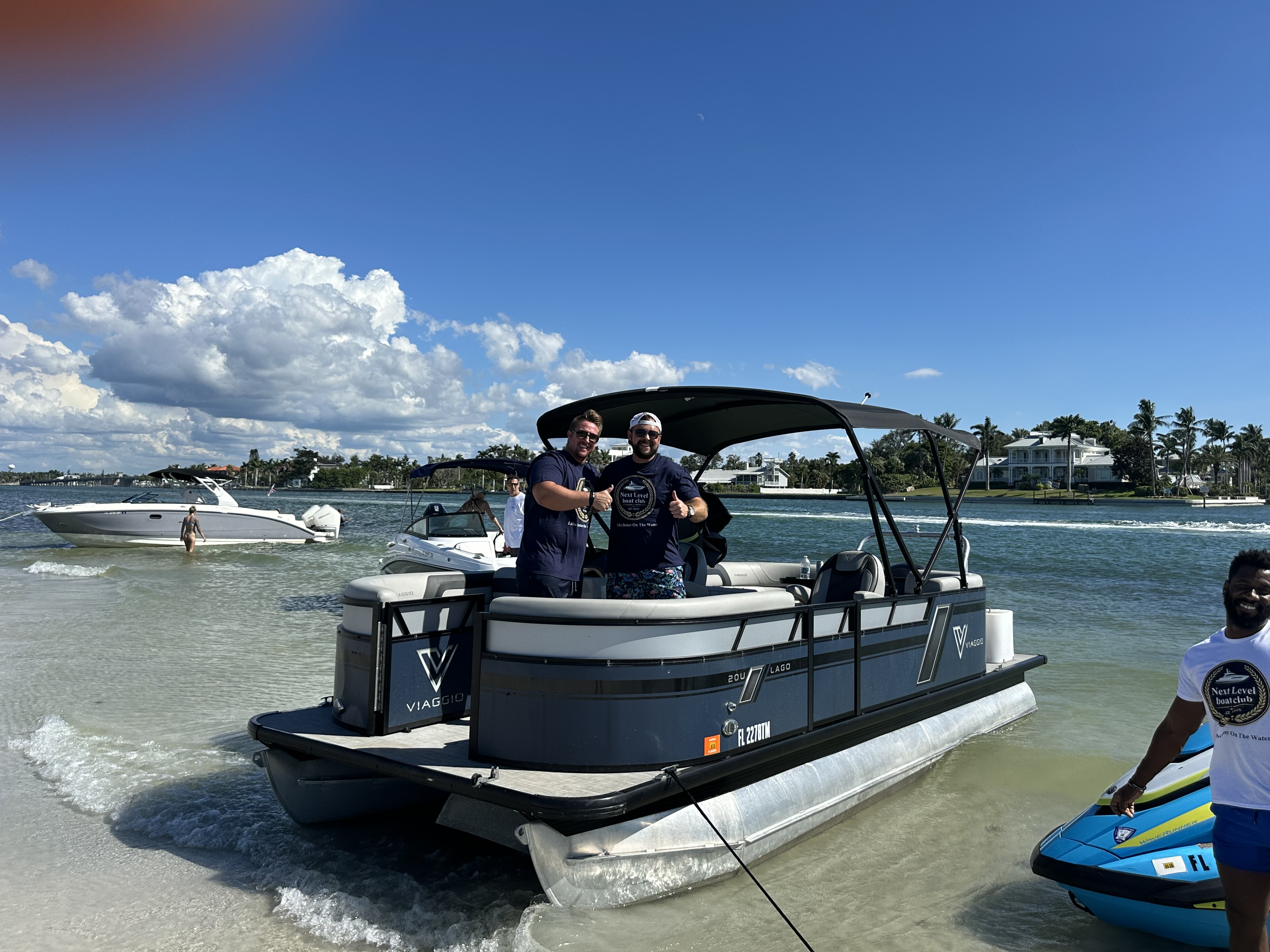 Two men on a pontoon boat, one man on jet ski